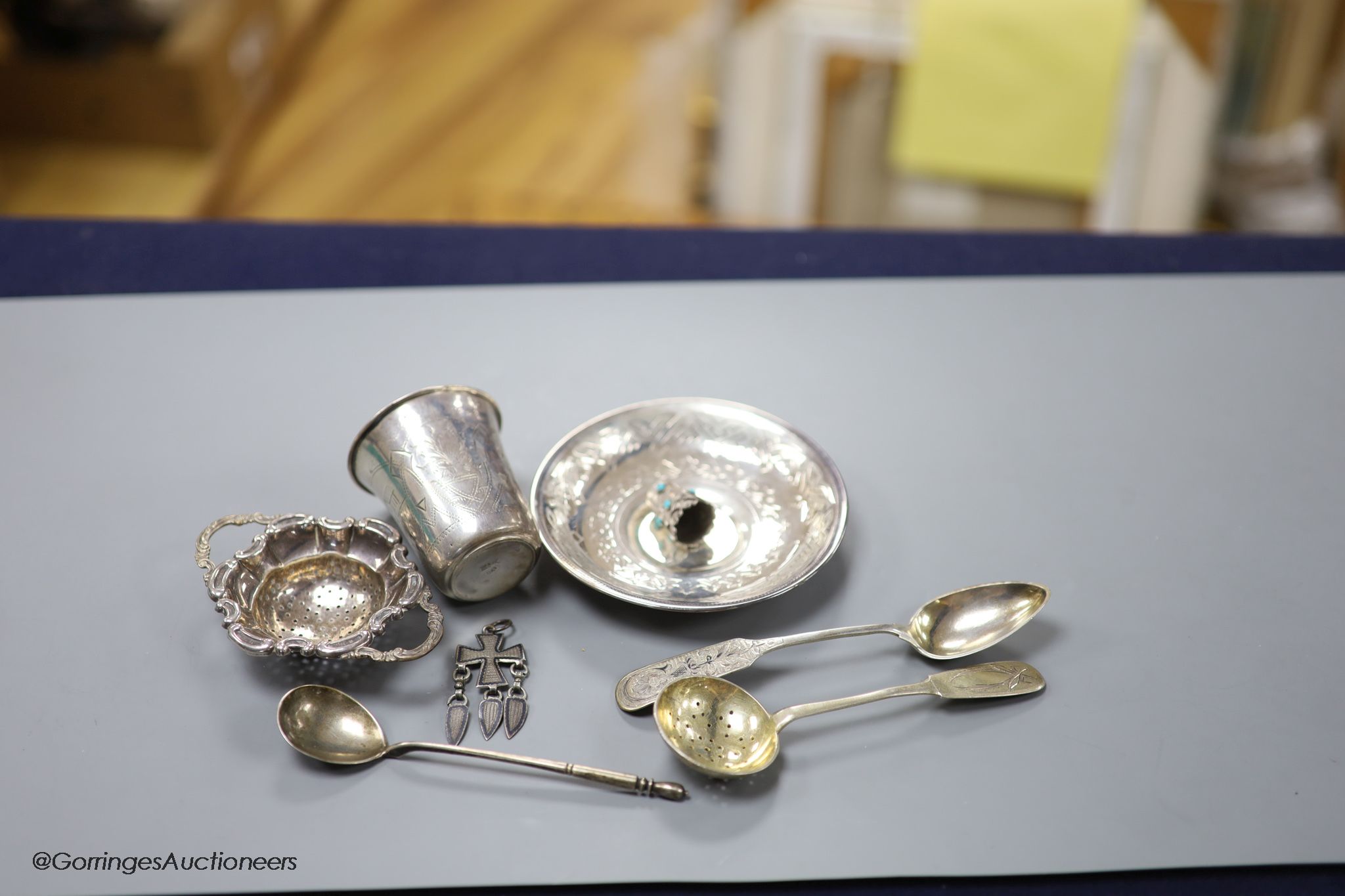 A late 19th century Russian engraved 84 zolotnik beaker, 1893, 63mm, a similar saucer, 1886, three assorted similar spoons, a white metal thimble and pendant and a German 835 tea strainer